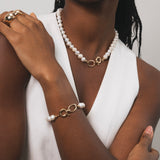 Femme noir qui porte une parrure raffinée qui associe la modernité du doré à la pureté des perles d'eau douces. Chaque piece est pensée pour apporter éclat et élégance, tout en restant facile à porter au quotidien. Le bracelet est raffiné combinant maillons dorés et perles, pour une harmonie parfaite avec le collier. 