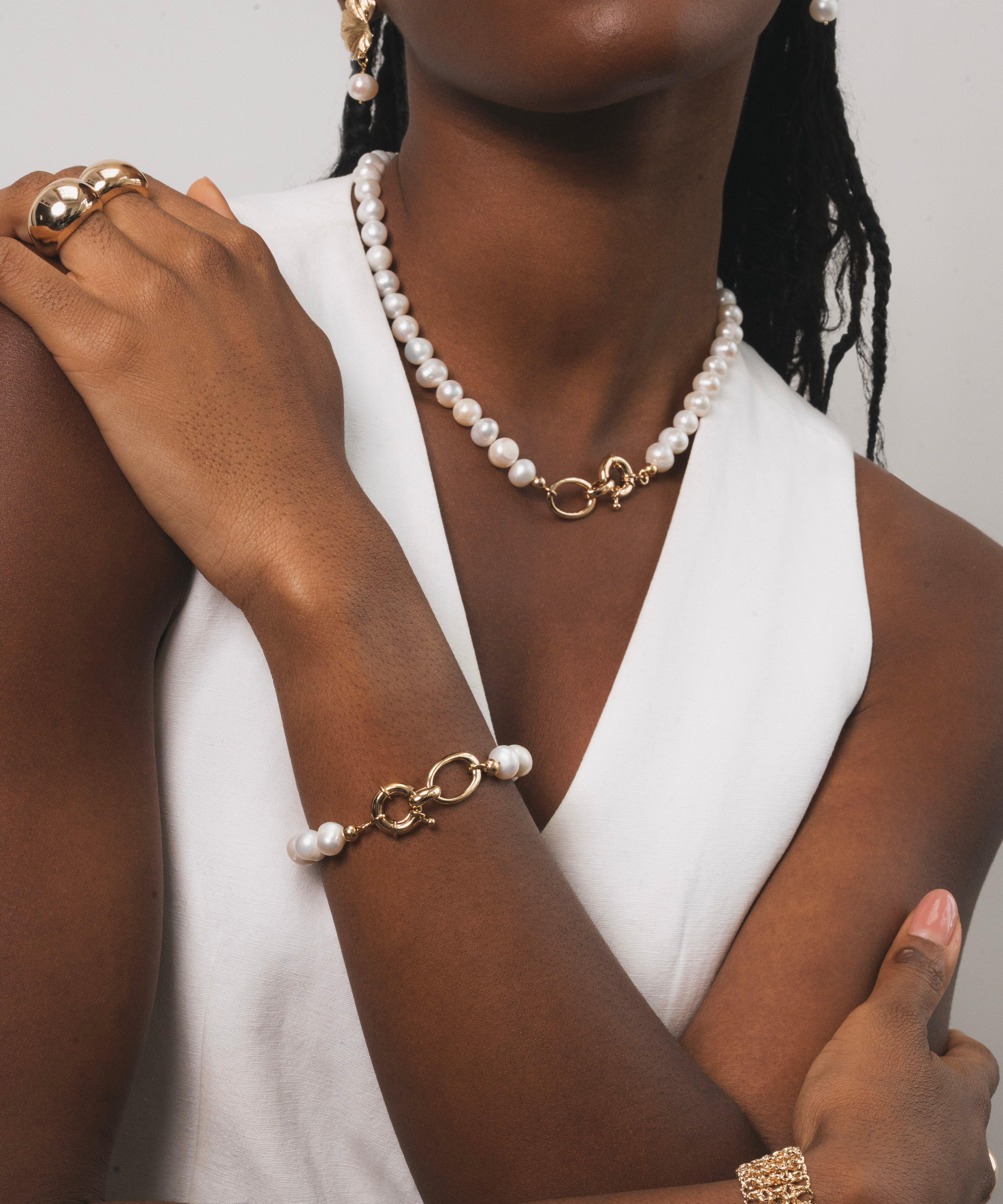 Femme noir qui porte une parrure raffinée qui associe la modernité du doré à la pureté des perles d'eau douces. Chaque piece est pensée pour apporter éclat et élégance, tout en restant facile à porter au quotidien. Le bracelet est raffiné combinant maillons dorés et perles, pour une harmonie parfaite avec le collier. 