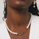 Femme noire qui porte un collier en perles d'eau douce avec des détails dorés en plaqué or. Ce collier a comme particularité un gros fermoir, ce qui fait toute la classe de ce bijou. On peut aussi apercevoir les boucles d'oreilles avec une base dorée en plaqué or ainsi qu'une perle d'eau douce pendante en finition.