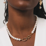 Femme noire qui porte un collier en perles d'eau douce avec des détails dorés en plaqué or. Ce collier a comme particularité un gros fermoir, ce qui fait toute la classe de ce bijou. On peut aussi apercevoir les boucles d'oreilles avec une base dorée en plaqué or ainsi qu'une perle d'eau douce pendante en finition.