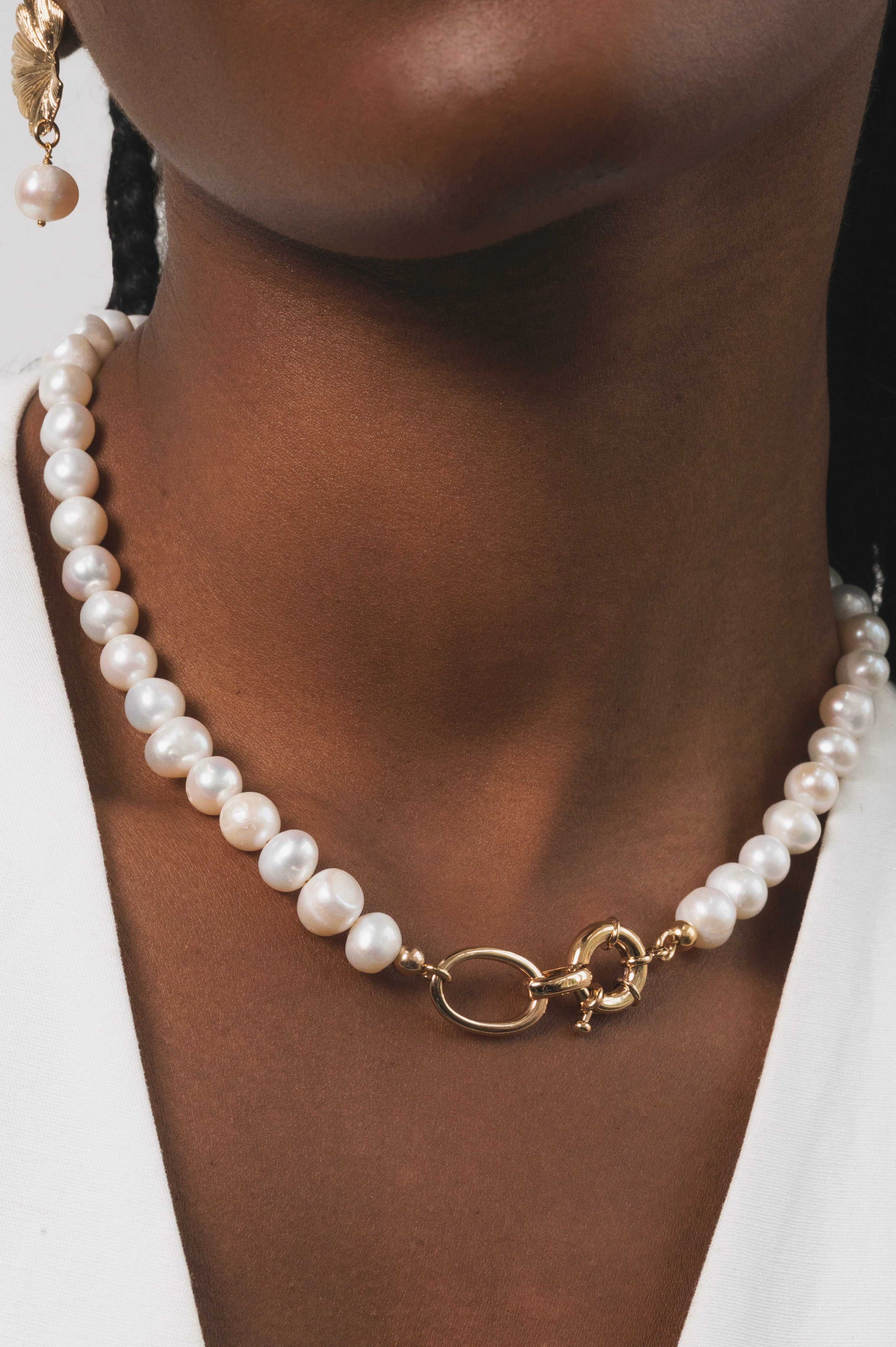Femme noire qui porte un collier en perles d'eau douce avec des détails dorés en plaqué or. Ce collier a comme particularité un gros fermoir, ce qui fait toute la classe de ce bijou. Ce collier est rafiner, elegant et surtout unique avec ses perles d'eau douces de formes ronde.