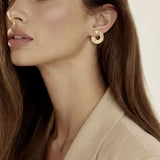 Jolie jeune femme chatain, peau blanche légèrement maquillée, fard à joue, maquillage nude, longs cheveux, yeux clairs, une oreille dégagée, qui laisse voir la boucle d'oreille parfaite, doré or, solaire , d'une taille idéale. Un rond de 2 cm comme un soleil rayonnant, un parfait cadeau à offrir, réussite garantié