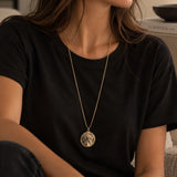jaune femme chatain qui porte un tee shirt noir et dessus un sautoir long doré représentant Marianne visage de la république française